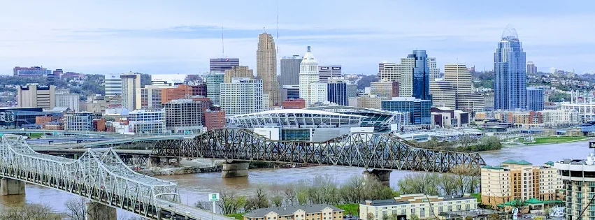 Wide view of the Cincinnati skyline with a stadium, two bridges and the Ohio River.