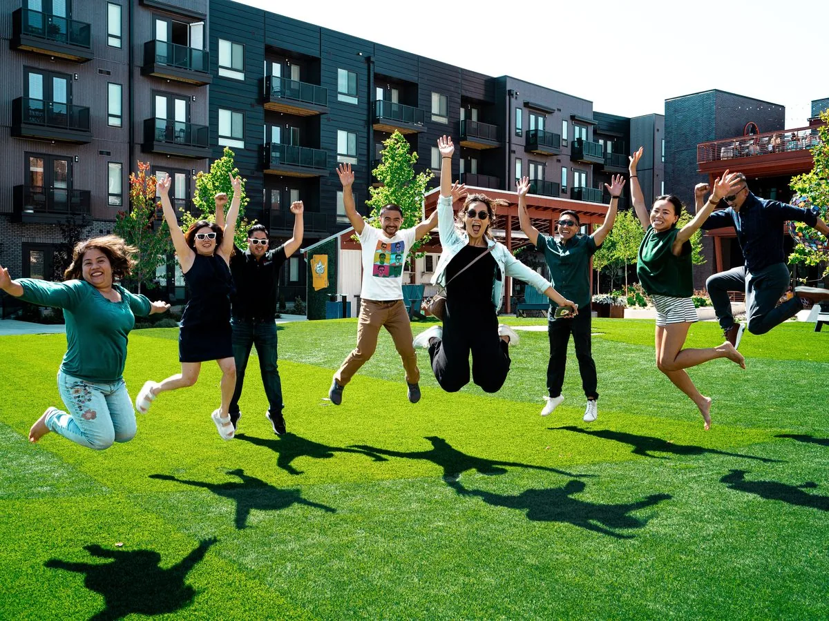 Cincinnati Field Trip participants jumping together on a lawn outside an apartment community.